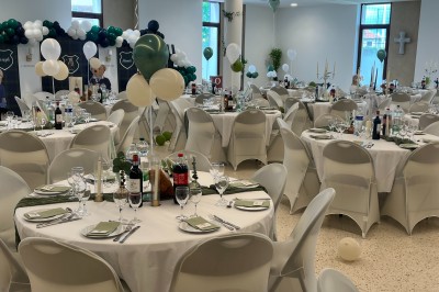 Table ronde dressée pour un événement, avec nappes blanches, serviettes vertes, bougies et boissons disposées au centre.