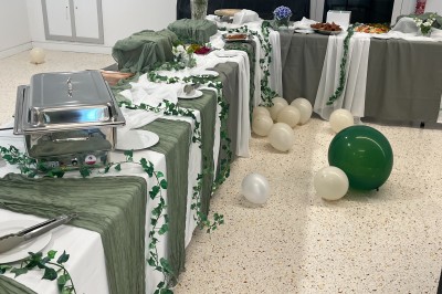 Table ronde dressée pour un événement, avec nappes blanches, serviettes vertes, bougies et boissons disposées au centre.