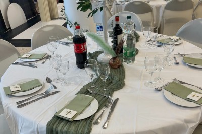 Table ronde dressée pour un événement, avec nappes blanches, serviettes vertes, bougies et boissons disposées au centre.