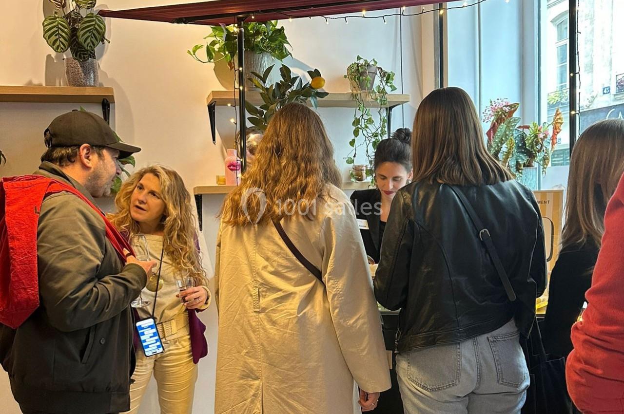 Un groupe de personnes échange devant un stand décoré de plantes dans un espace intérieur lumineux.