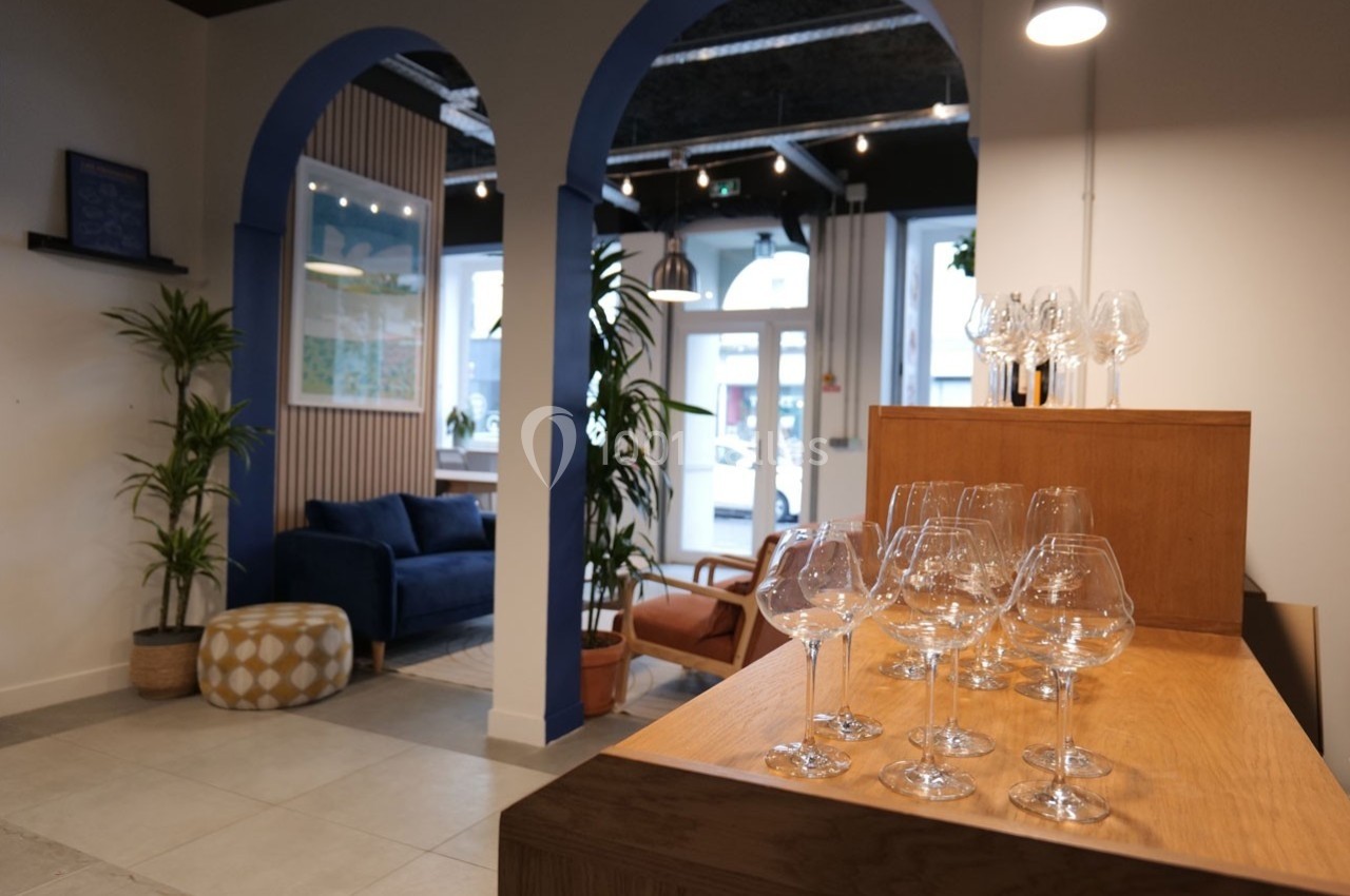 Espace intérieur lumineux avec arches bleues, canapé, plantes et verres à vin disposés sur un comptoir en bois.