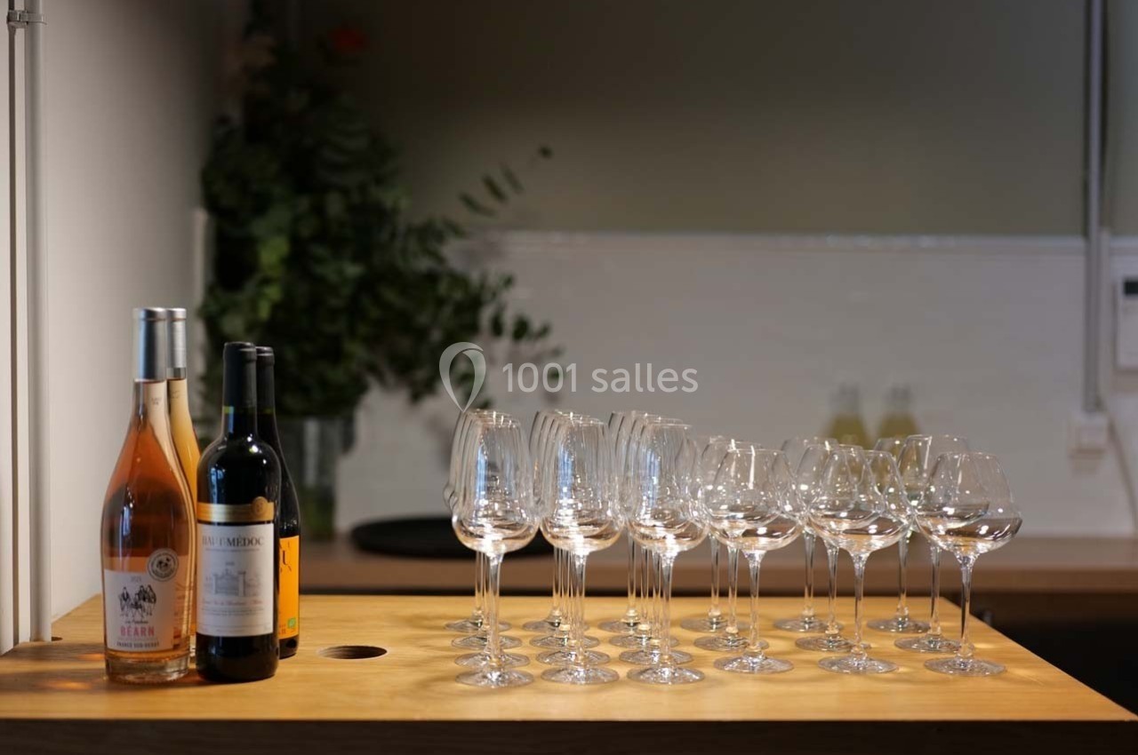 Bouteilles de vin et rangée de verres à pied vides sur un comptoir en bois, avec un fond flou de cuisine.