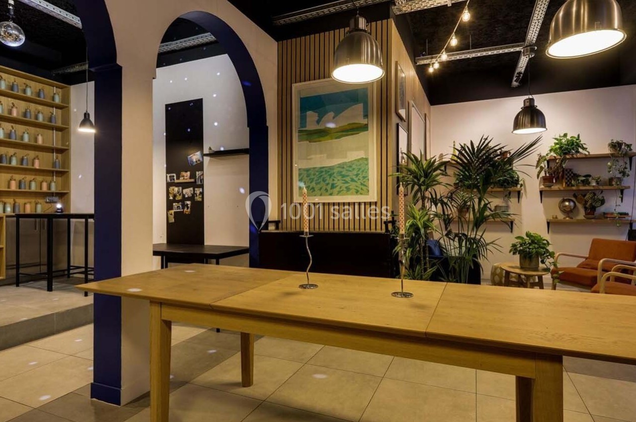 Espace intérieur moderne avec table en bois, plantes, étagères décorées et éclairage suspendu.