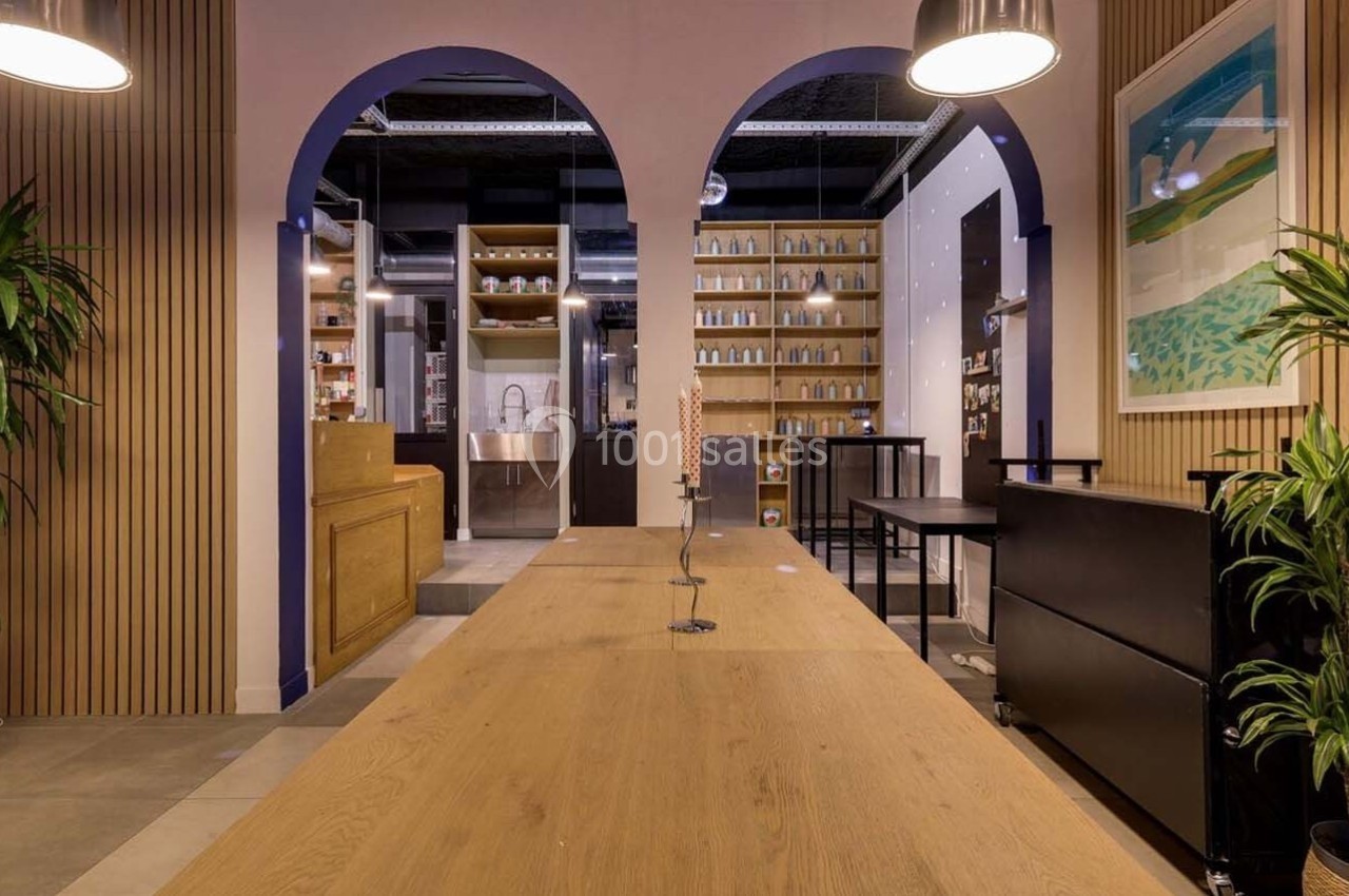 Intérieur d'un espace moderne avec arches, plantes, étagères remplies et un grand plan de travail en bois clair.