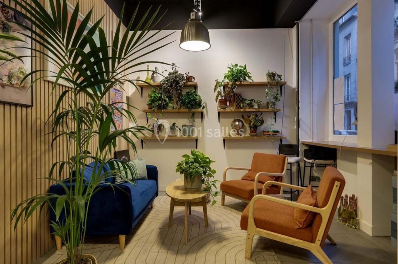 Espace intérieur chaleureux avec canapé bleu, fauteuils orange, plantes et étagères décorées sur un mur en bois.