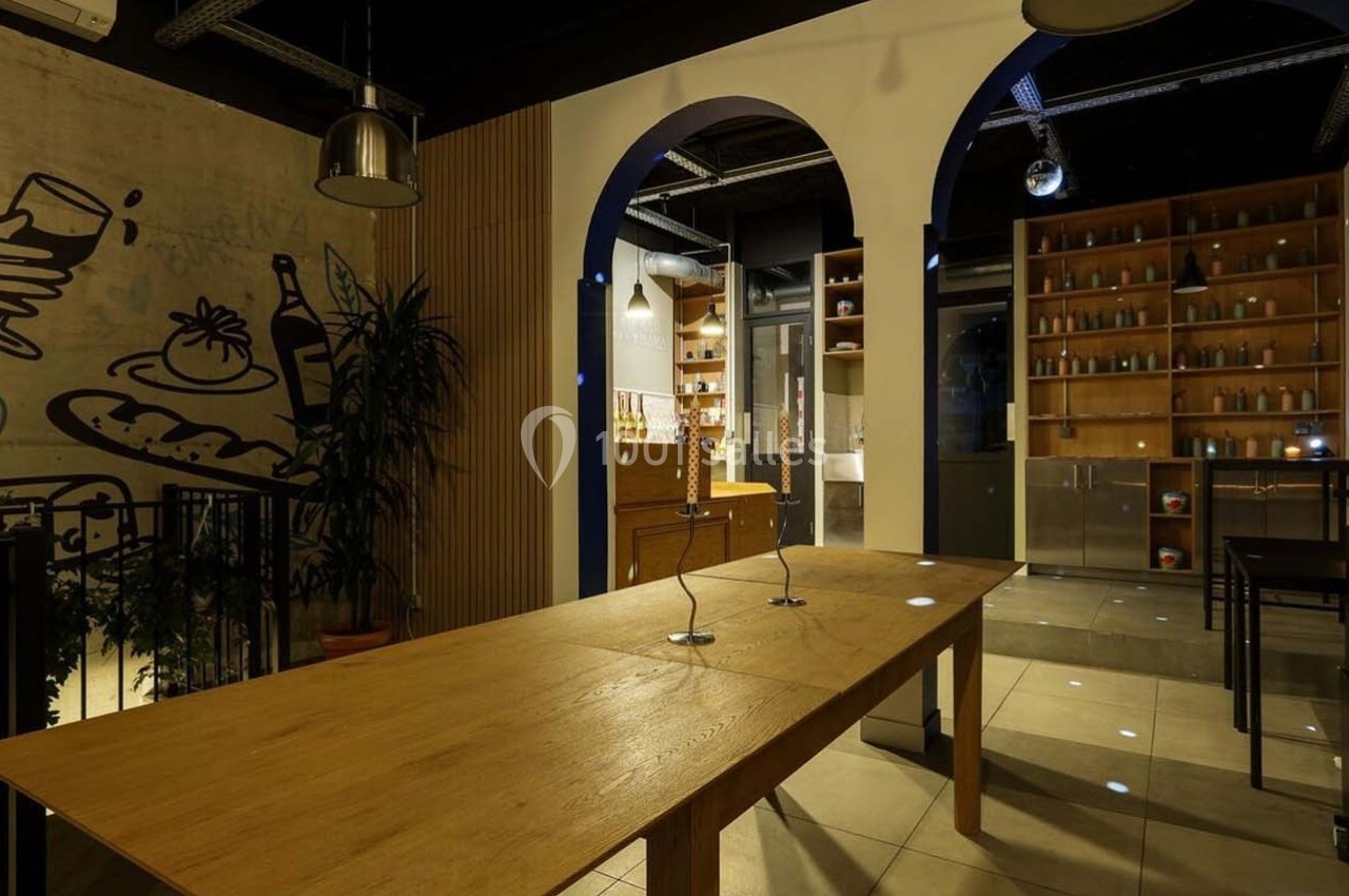 Salle moderne avec table en bois, étagères remplies de bouteilles, fresque murale et éclairage tamisé.