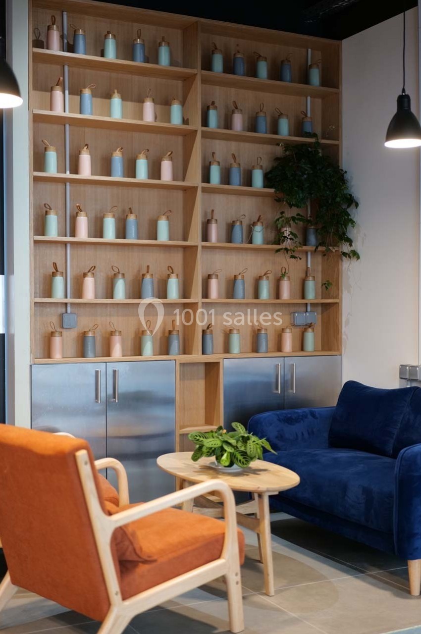 Salon moderne avec fauteuils colorés, table basse en bois, étagères remplies de bouteilles décoratives et plantes.