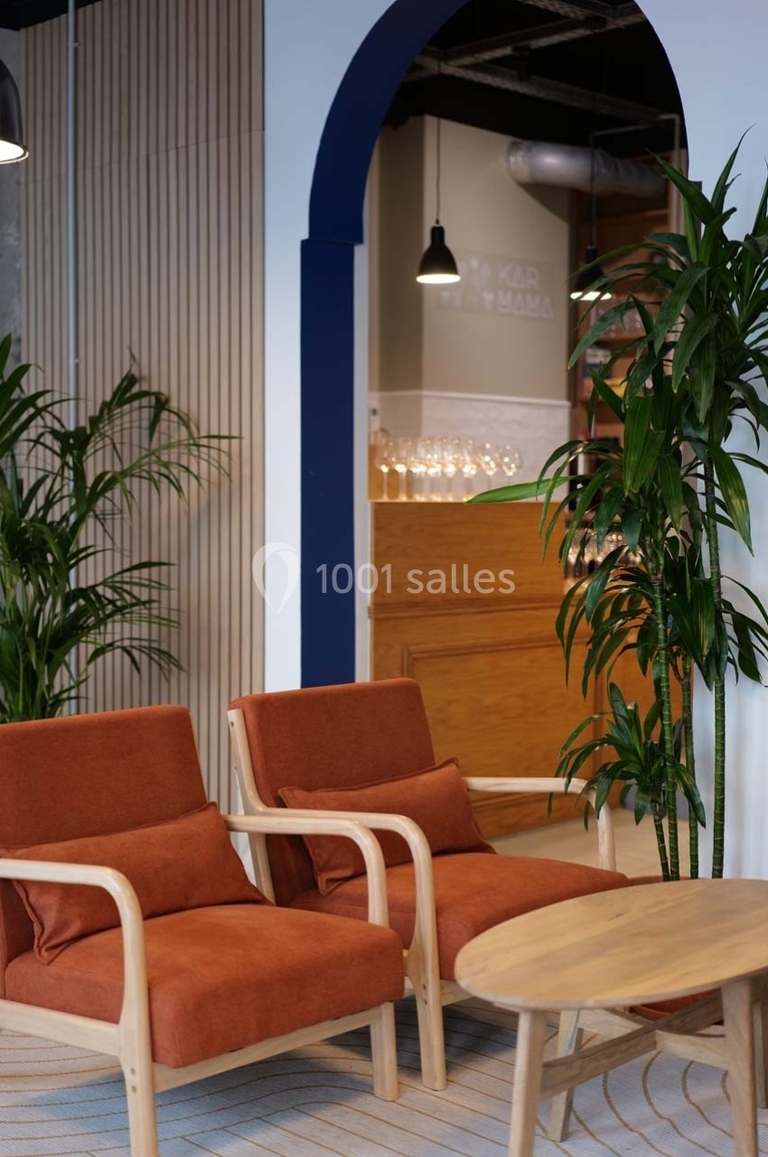 Deux fauteuils orange avec coussins, une table basse en bois et des plantes dans un espace intérieur moderne.