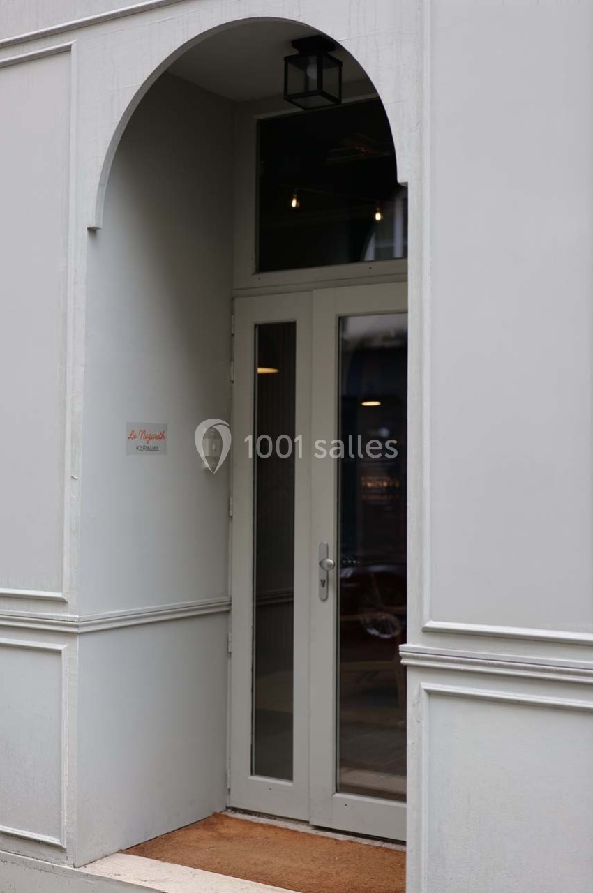 Entrée discrète avec porte vitrée encadrée d'un arc, mur gris clair et petite lampe suspendue.