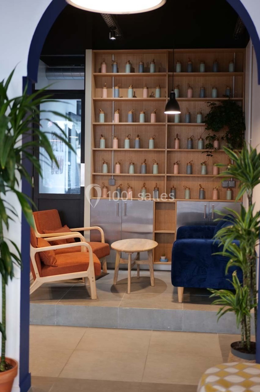 Espace salon avec fauteuils colorés, table basse en bois et étagère garnie de bouteilles décoratives.