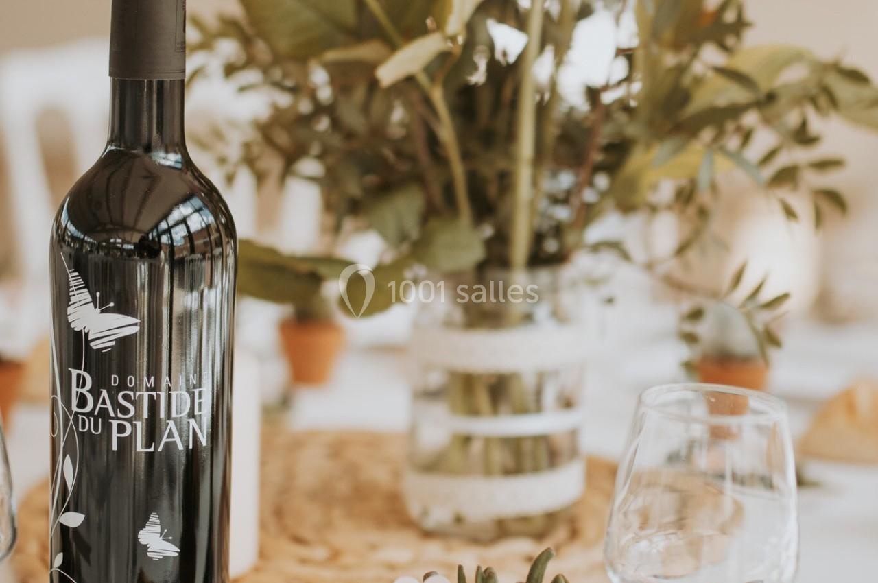 Bouteille de vin rouge posée sur une table décorée de fleurs, avec des verres, du pain et des olives.