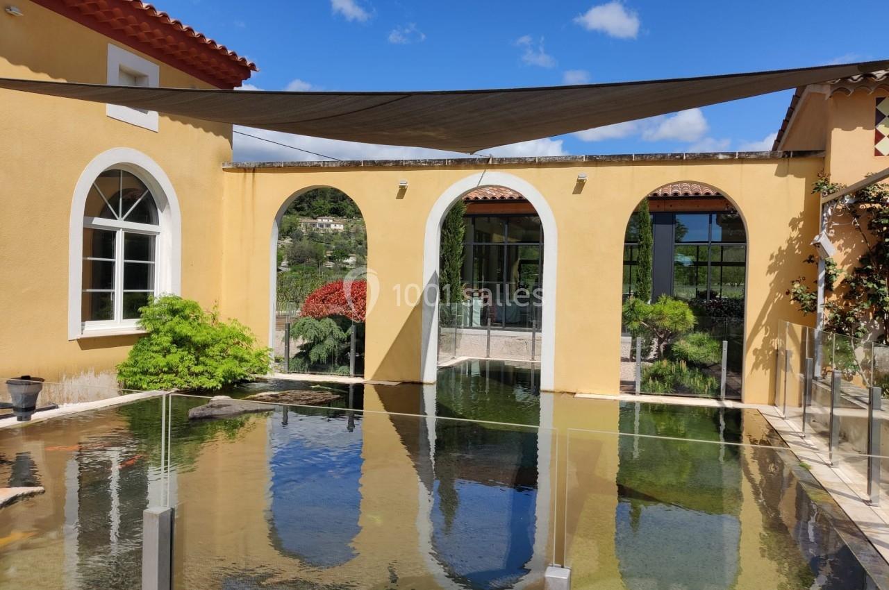Bassin d'eau calme entouré d'arches jaunes, végétation et voiles d'ombrage sous un ciel bleu.