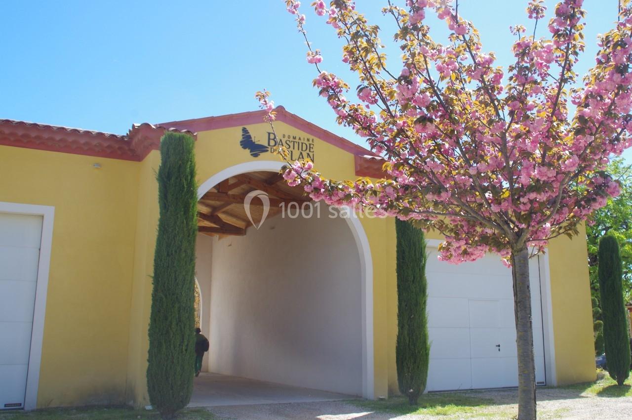 Entrée voûtée d'un bâtiment jaune avec un arbre en fleurs au premier plan, sous un ciel bleu.