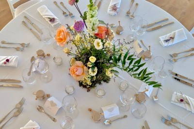 Terrasse extérieure avec tables dressées sous des parasols, entourée de végétation et de fleurs au premier plan.