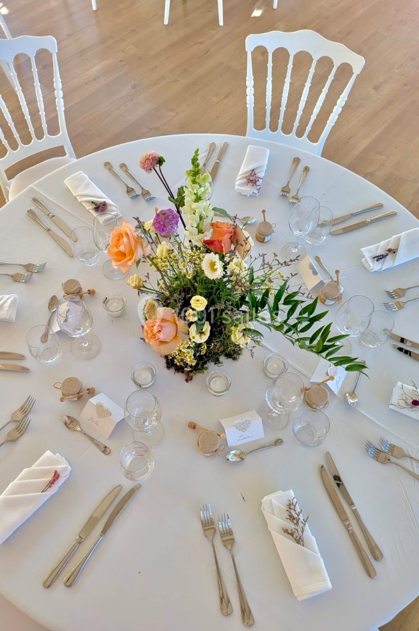 Table ronde décorée pour un événement, avec nappe blanche, couverts, serviettes pliées et centre de table floral.