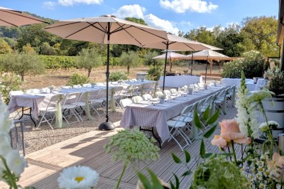 Terrasse extérieure avec tables dressées sous des parasols, entourée de végétation et de fleurs au premier plan.