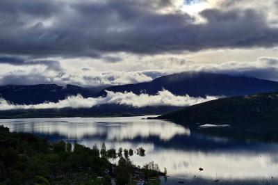 Vue d'un lac entouré de collines verdoyantes, avec quelques bateaux amarrés et un ciel partiellement nuageux.