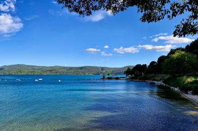 Vue d'un lac entouré de collines verdoyantes, avec quelques bateaux amarrés et un ciel partiellement nuageux.