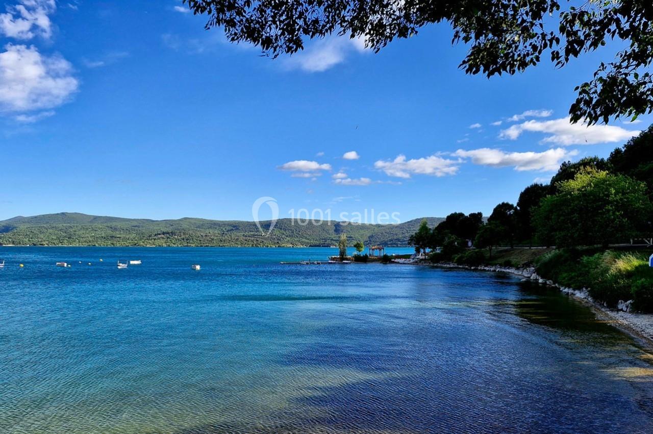 Vue d'un lac entouré de collines verdoyantes, avec quelques bateaux amarrés et un ciel partiellement nuageux.