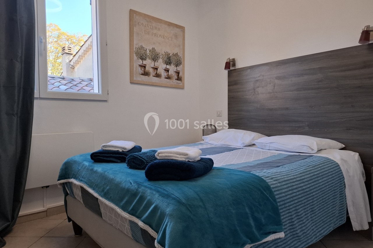 Lit double avec draps et couvertures bleues, deux serviettes pliées, dans une chambre lumineuse avec fenêtre et décoration…