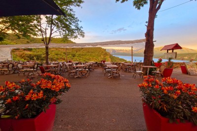Vue d'un lac entouré de collines verdoyantes, avec quelques bateaux amarrés et un ciel partiellement nuageux.