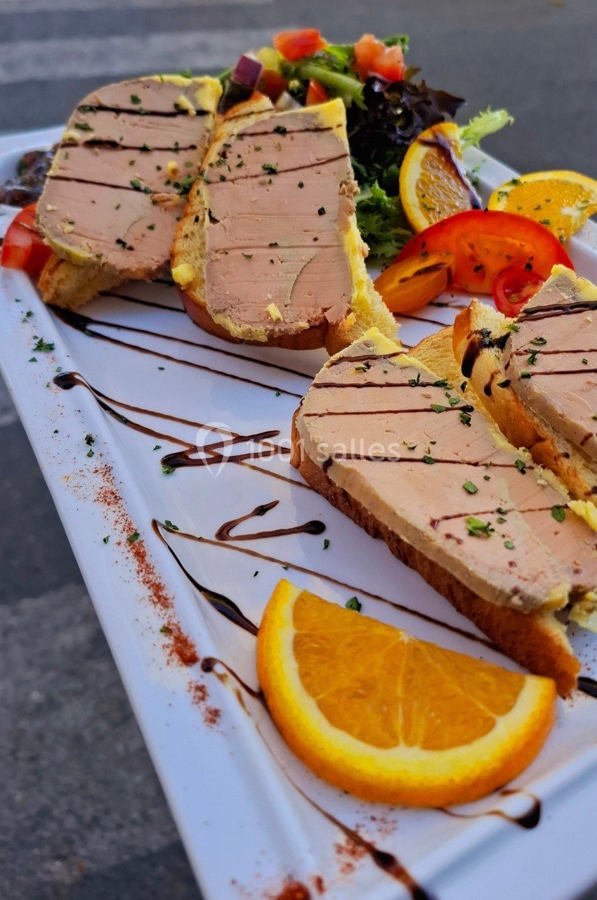 Tranches de foie gras sur pain grillé, accompagnées de salade, tomates et rondelles d'orange sur une assiette blanche.