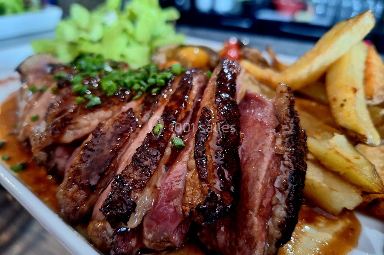 Tranches de magret de canard grillé avec frites et salade, servies sur une assiette dans un cadre de restaurant.