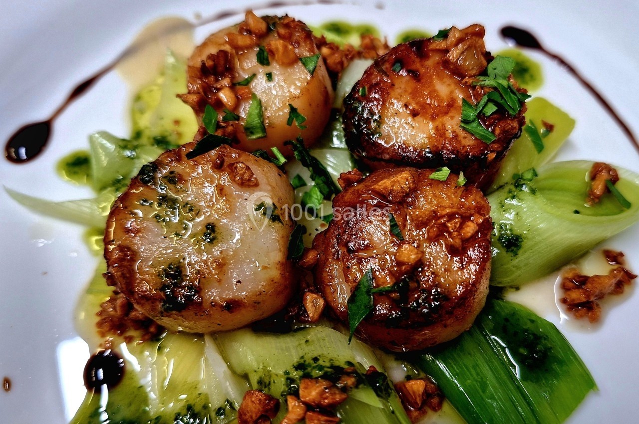 Noix de Saint-Jacques poêlées servies sur un lit de poireaux avec une garniture d'herbes, d'ail et de sauce.