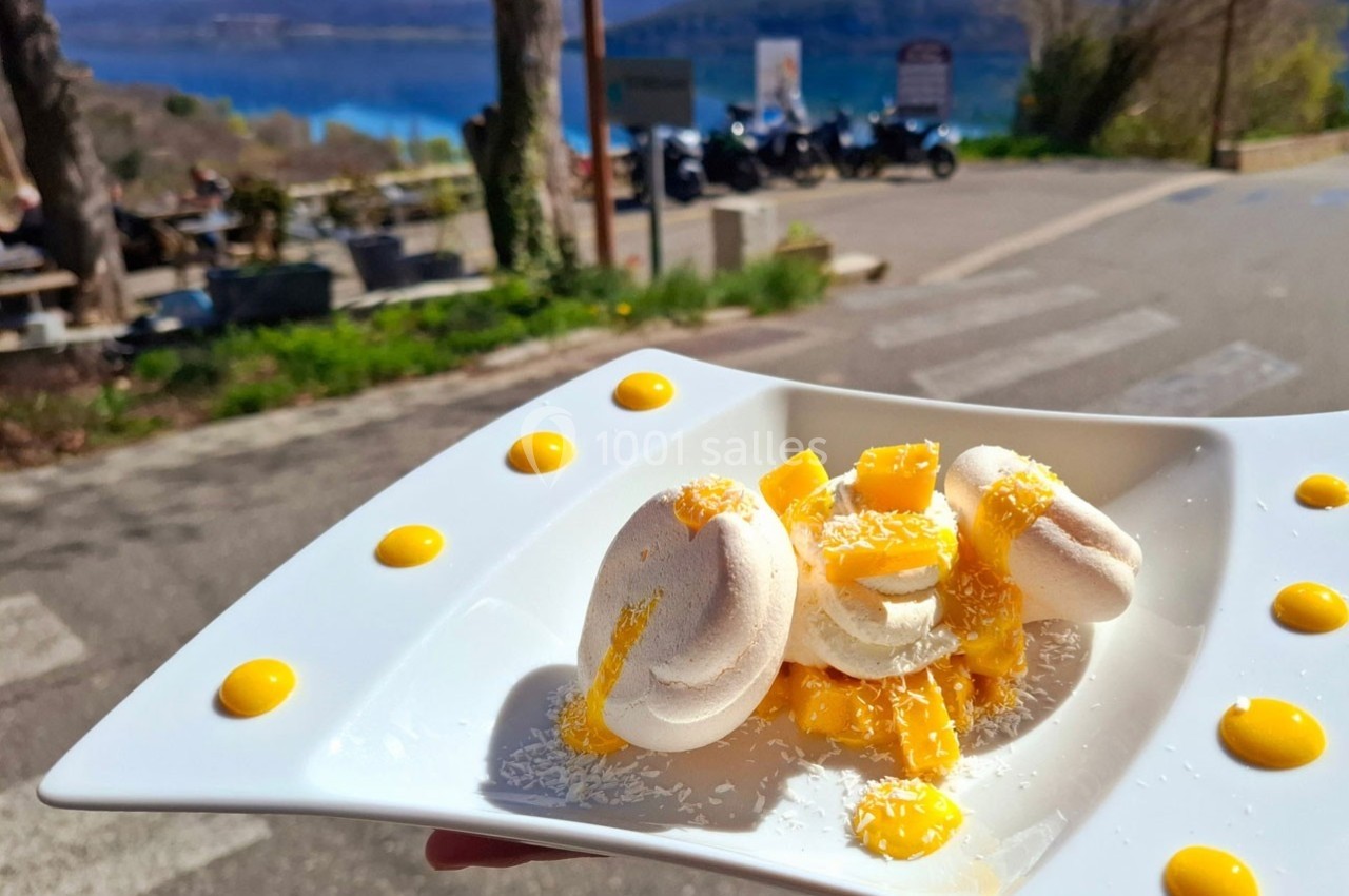 Assiette de dessert avec des meringues, morceaux de mangue et sauce fruitée, présentée en extérieur près d'un lac.