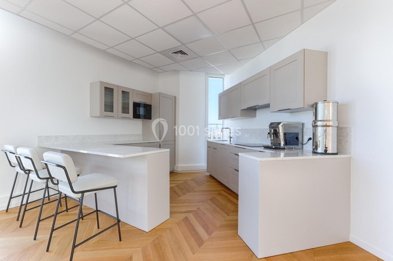 Cuisine moderne avec meubles gris, plan de travail en marbre, tabourets hauts et sol en parquet clair.