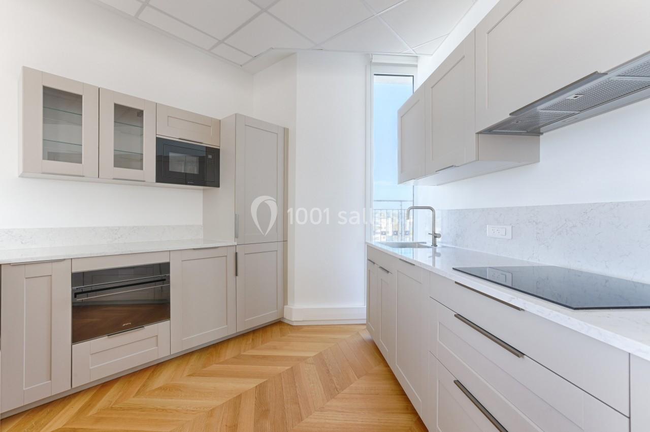 Cuisine moderne avec meubles beige clair, plan de travail en marbre blanc, parquet en bois et fenêtre lumineuse.