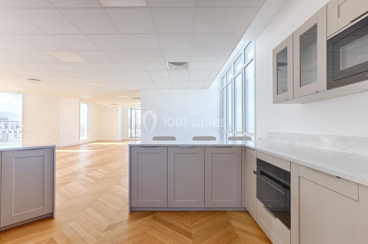 Cuisine moderne lumineuse avec meubles gris, plan de travail en marbre, parquet en bois clair et grandes fenêtres.