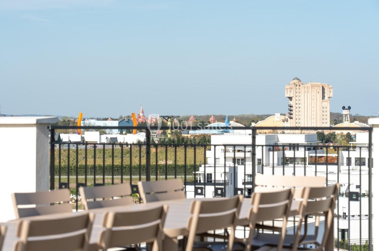 Vue depuis une terrasse avec des chaises, donnant sur des bâtiments et des attractions au loin sous un ciel dégagé.