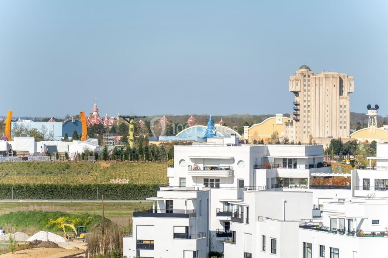 Vue sur des immeubles modernes au premier plan avec des attractions d'un parc d'attractions en arrière-plan.