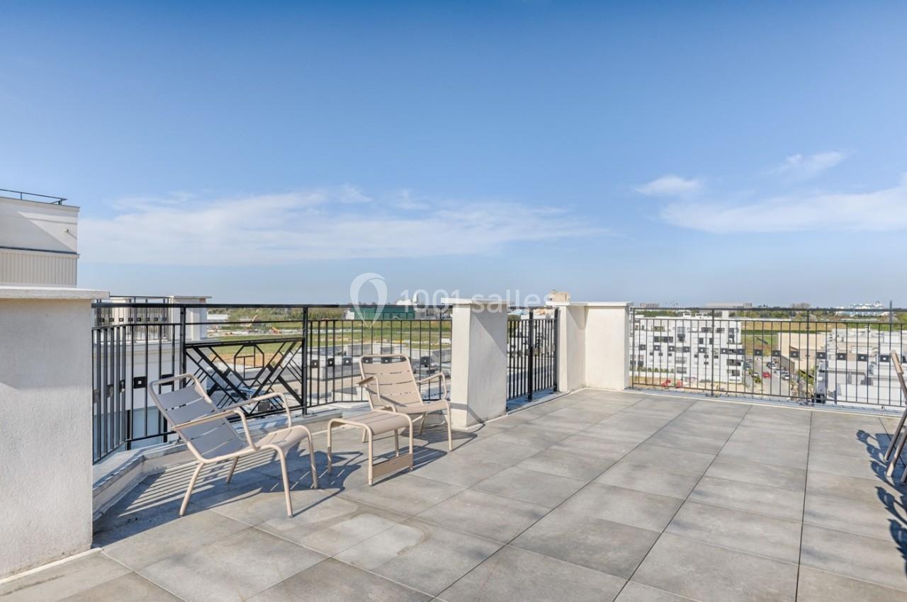 Terrasse spacieuse avec sol carrelé, chaises longues et vue dégagée sur des bâtiments et un ciel bleu.