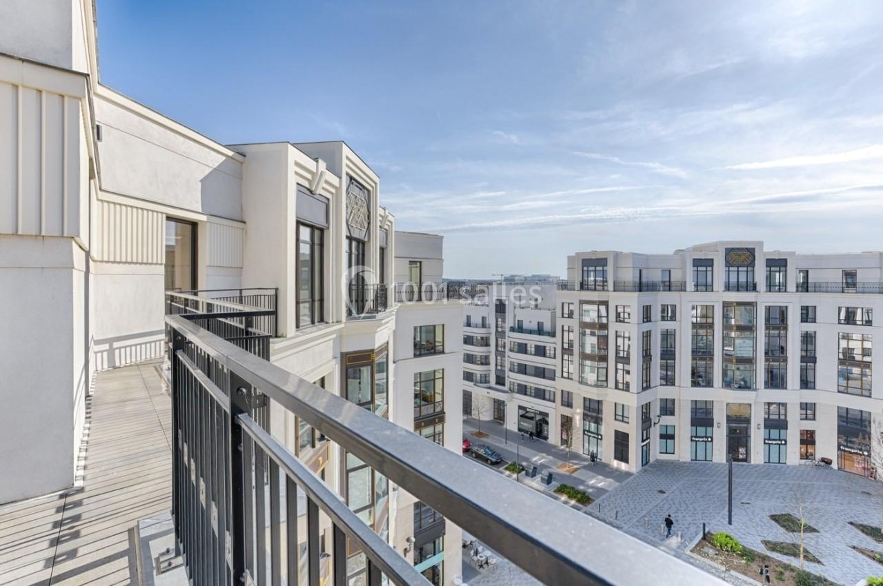 Vue depuis un balcon donnant sur une place entourée d'immeubles modernes sous un ciel dégagé.