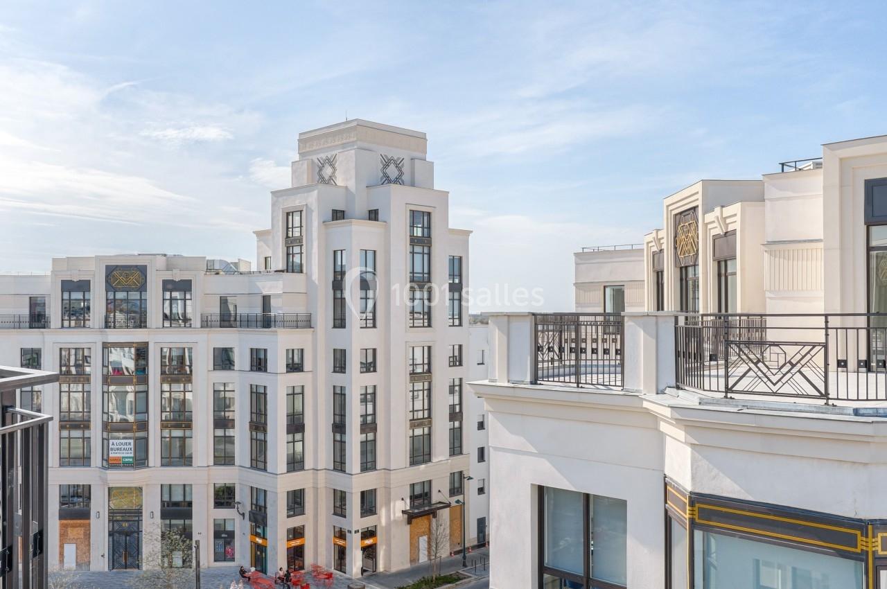 Vue sur des bâtiments modernes de style classique entourant une petite place avec des arbres en fleurs, sous un ciel dégagé.