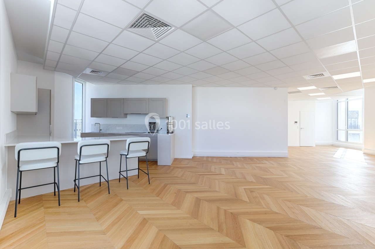 Cuisine moderne ouverte avec comptoir, tabourets hauts, parquet en chevrons et plafond à dalles blanches.