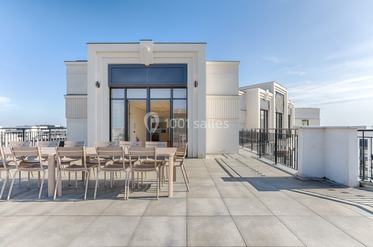 Terrasse spacieuse avec grande table en bois, chaises assorties et vue dégagée sous un ciel clair.