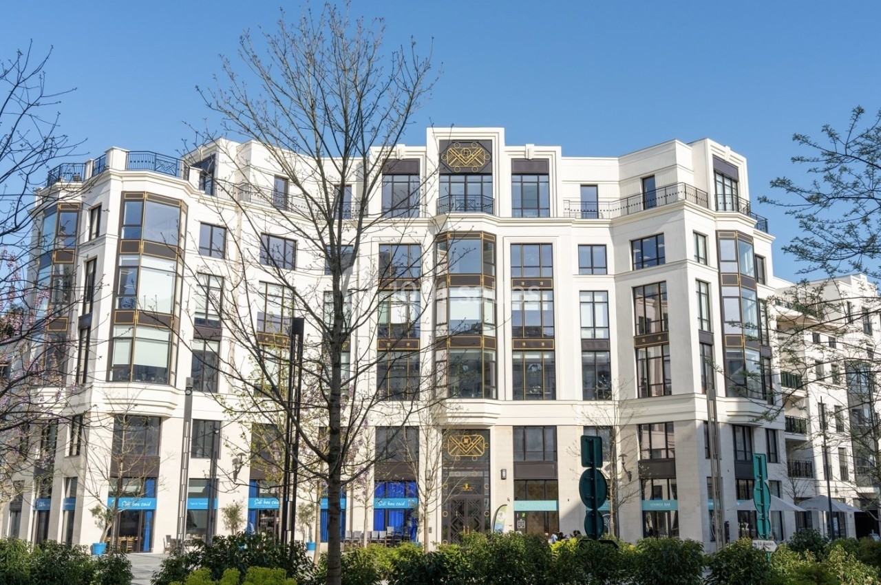 Façade d'un immeuble moderne avec grandes baies vitrées, entouré d'arbres et sous un ciel dégagé.