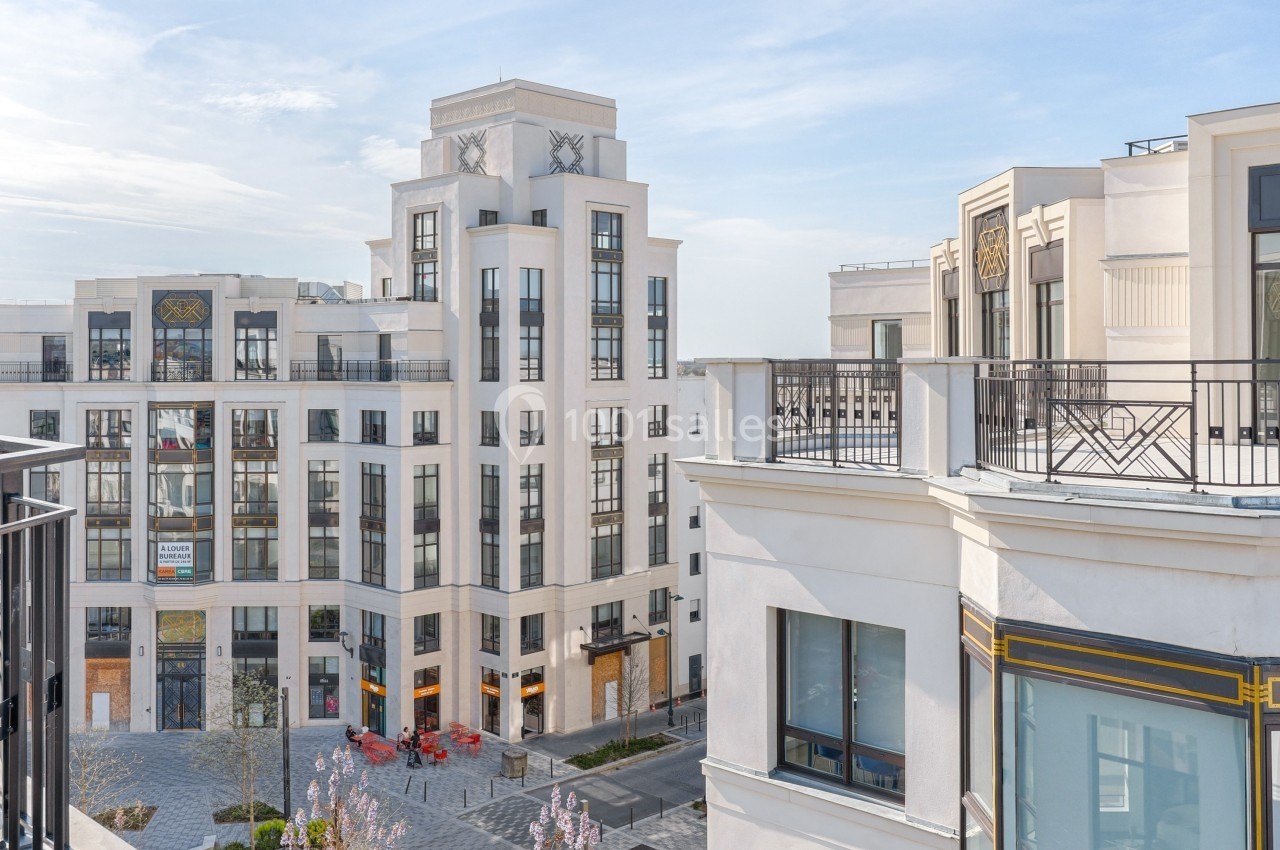 Vue d'un ensemble de bâtiments modernes en architecture classique, avec terrasses et une place piétonne en contrebas.