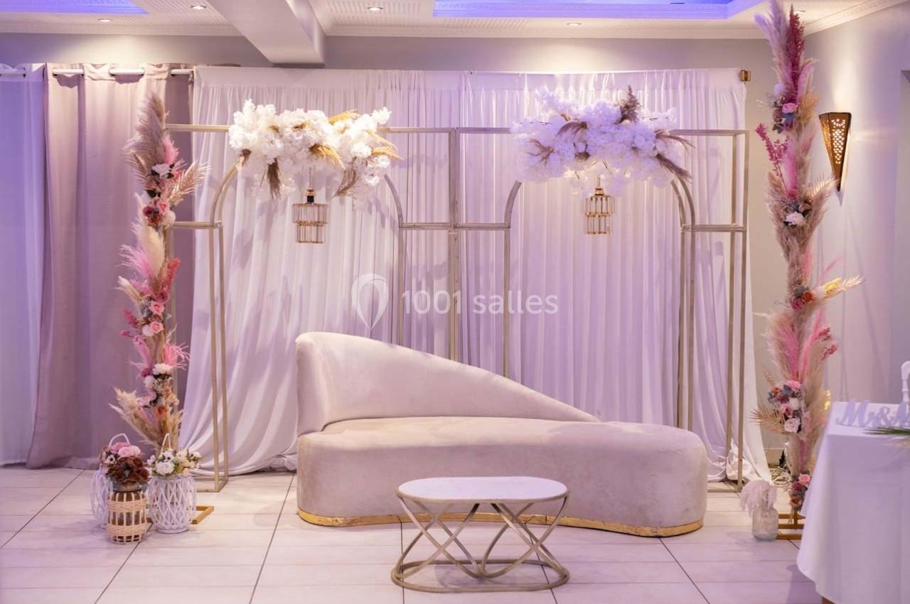 Canapé beige avec table basse ronde, décoré de fleurs séchées et artificielles sur une structure dorée devant un rideau…