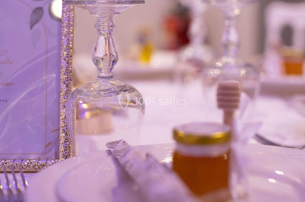 Un pot de miel avec une cuillère en bois posé sur une assiette blanche, entouré de verres et d'éléments de table.