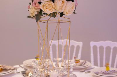 Centre de table avec structure dorée, bouquet de roses pastel et verres disposés sur une table dressée.