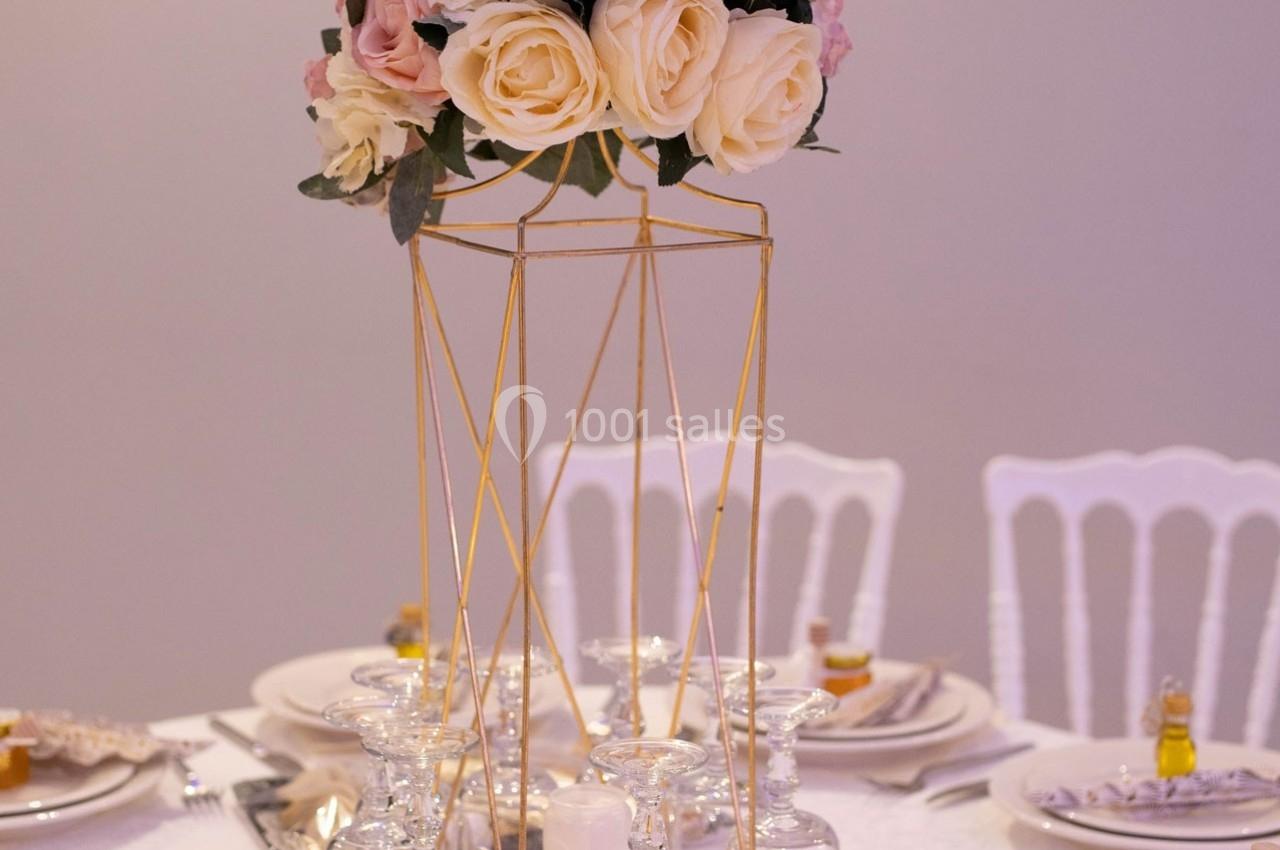 Centre de table avec structure dorée, bouquet de roses pastel et verres disposés sur une table dressée.