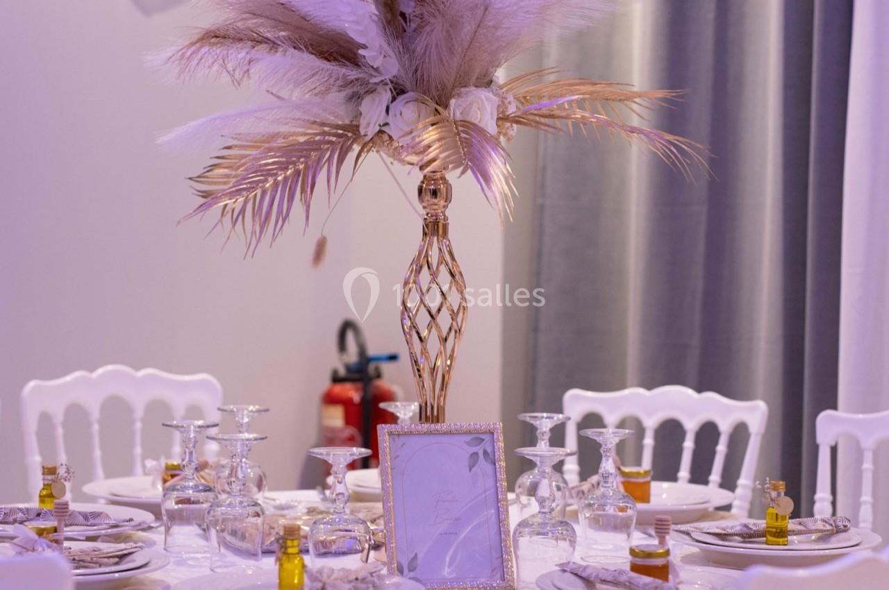 Centre de table élégant avec vase doré, plumes décoratives et vaisselle raffinée sur une table dressée.