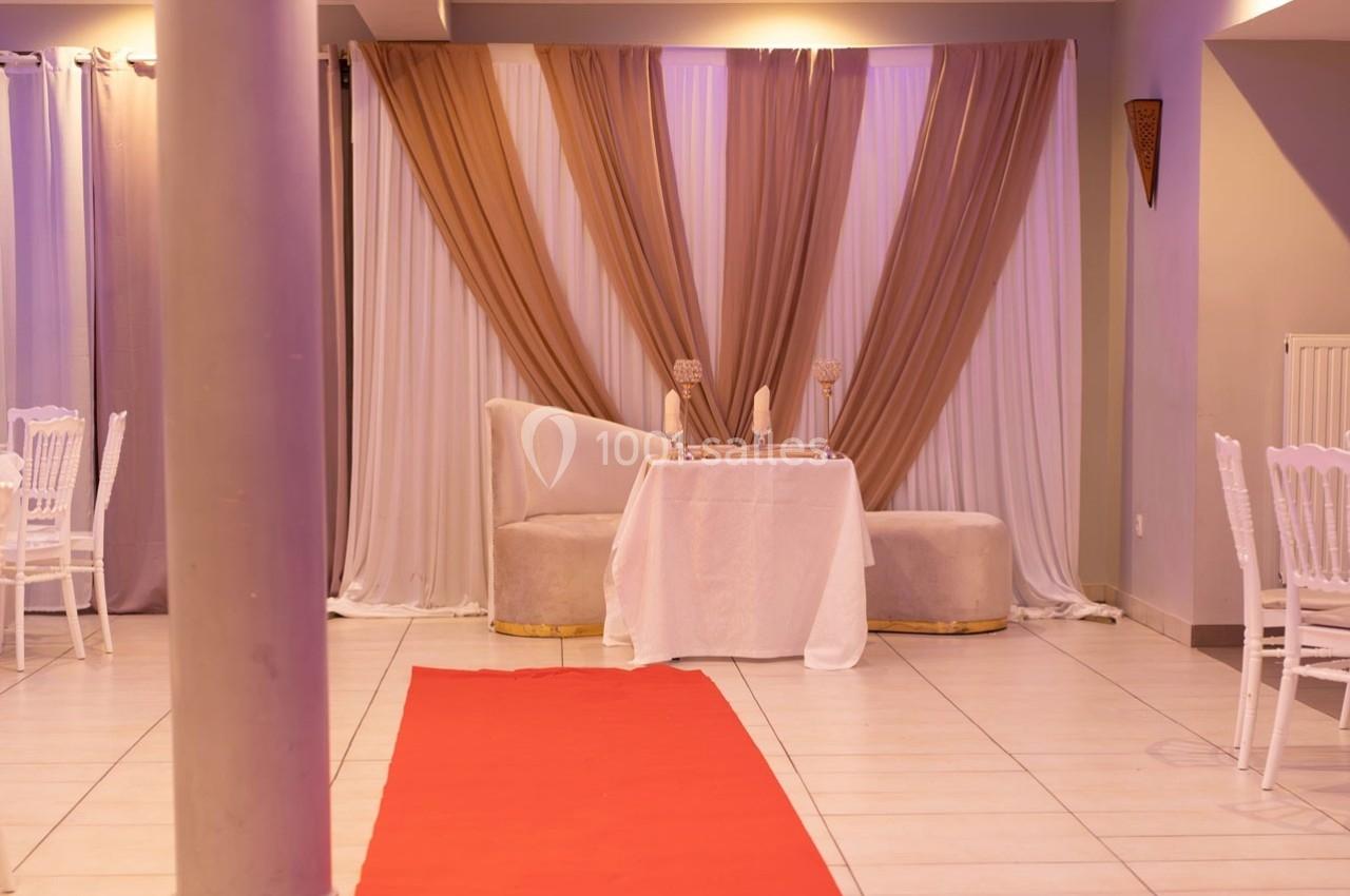 Table décorée avec deux fauteuils devant un rideau beige et blanc, tapis rouge au sol dans une salle lumineuse.
