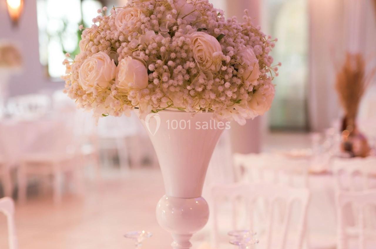Bouquet de roses blanches et gypsophiles dans un vase blanc, décorant une salle lumineuse avec des chaises blanches.