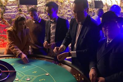 Table de jeu de casino avec tapis vert numéroté et porte-gobelets intégrés, entourée de personnes debout.