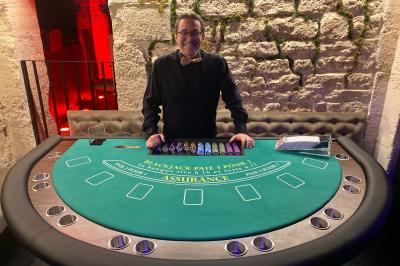 Table de jeu de casino avec tapis vert numéroté et porte-gobelets intégrés, entourée de personnes debout.